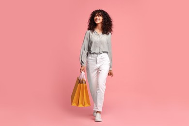 Smiling woman with colorful shopping bags on pink background