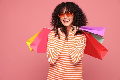 Smiling woman with colorful shopping bags on pink background