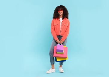 Smiling woman with colorful shopping bags on light blue background