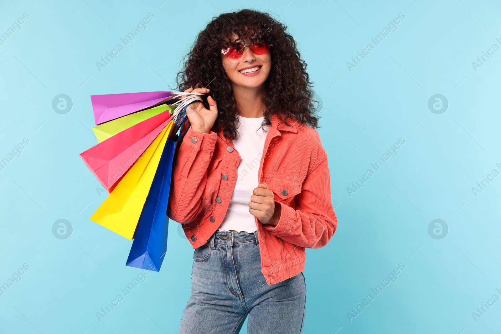 Photo of Smiling woman with colorful shopping bags on light blue background