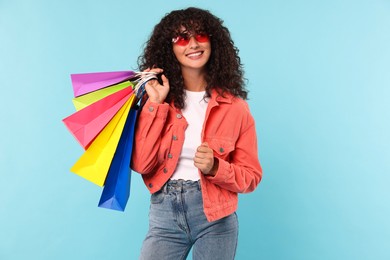 Smiling woman with colorful shopping bags on light blue background