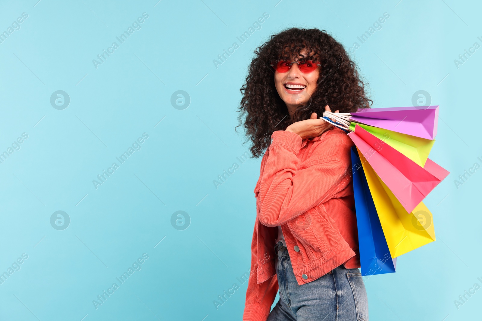 Photo of Smiling woman with colorful shopping bags on light blue background. Space for text