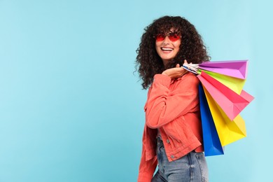 Photo of Smiling woman with colorful shopping bags on light blue background. Space for text