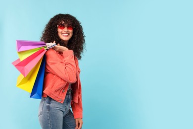 Smiling woman with colorful shopping bags on light blue background. Space for text