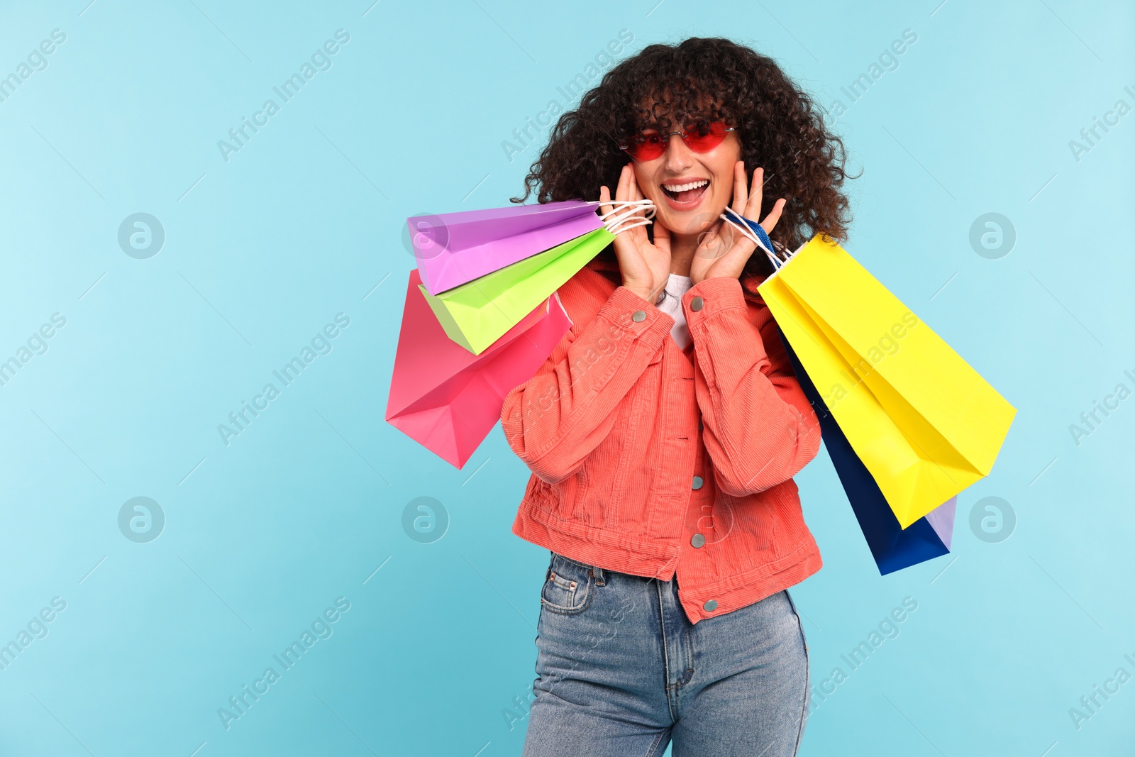 Photo of Happy woman with colorful shopping bags on light blue background. Space for text