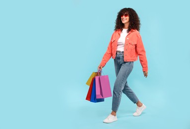 Photo of Smiling woman with colorful shopping bags on light blue background. Space for text