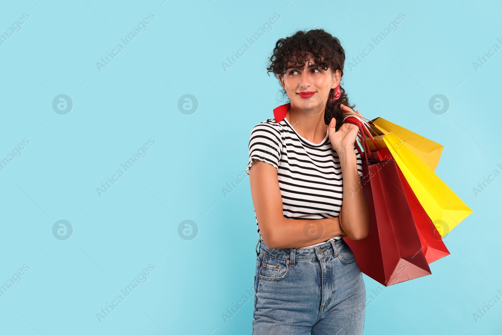 Photo of Beautiful woman with colorful shopping bags on light blue background. Space for text