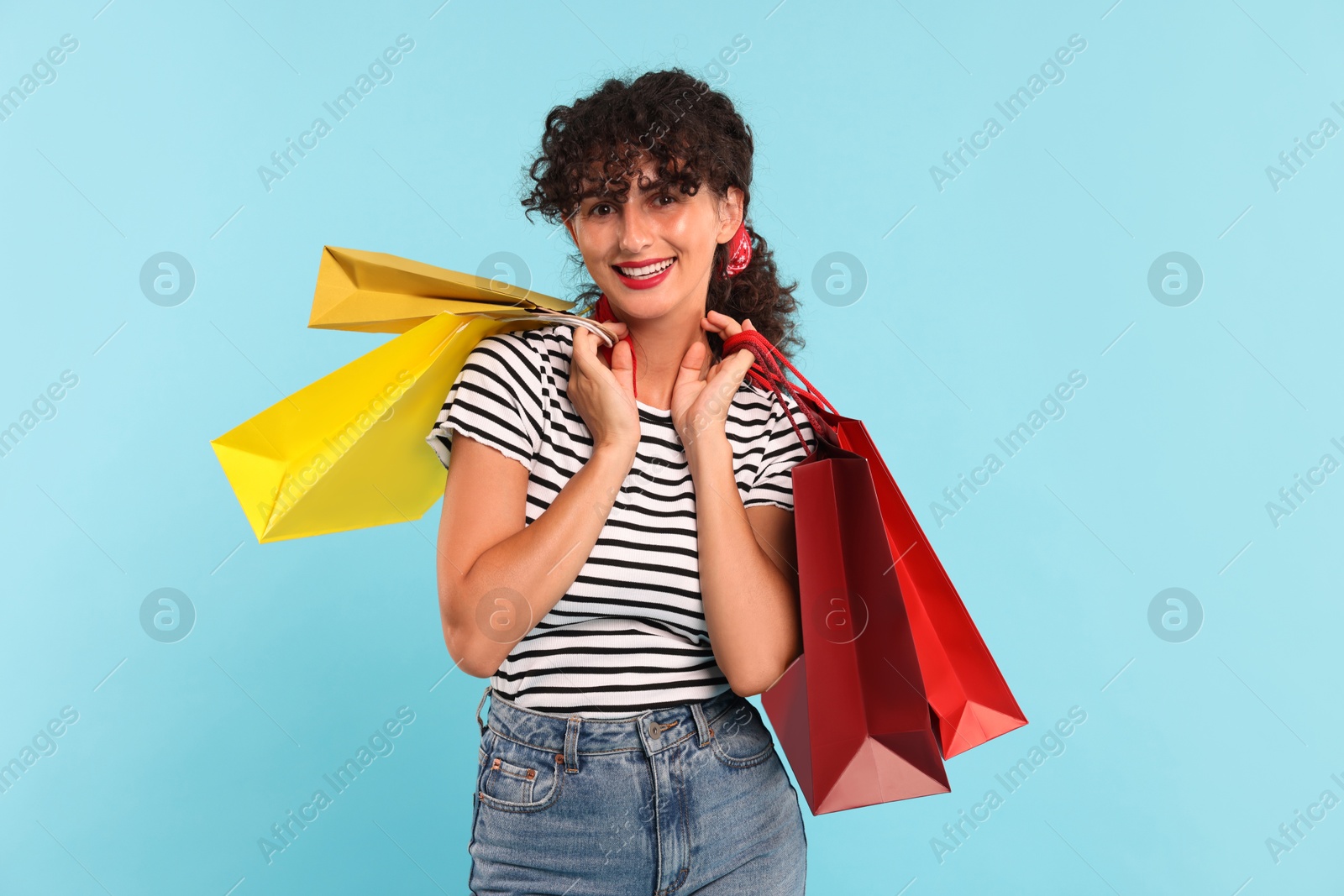 Photo of Smiling woman with colorful shopping bags on light blue background