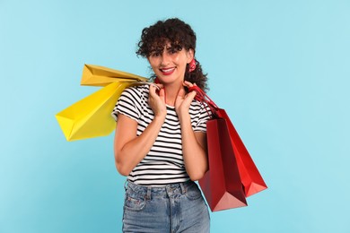 Smiling woman with colorful shopping bags on light blue background