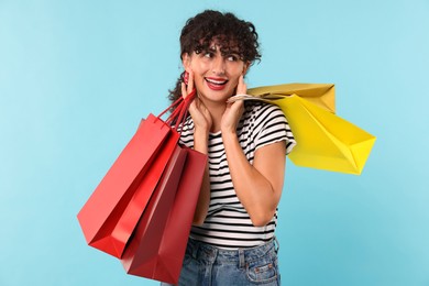 Smiling woman with colorful shopping bags on light blue background