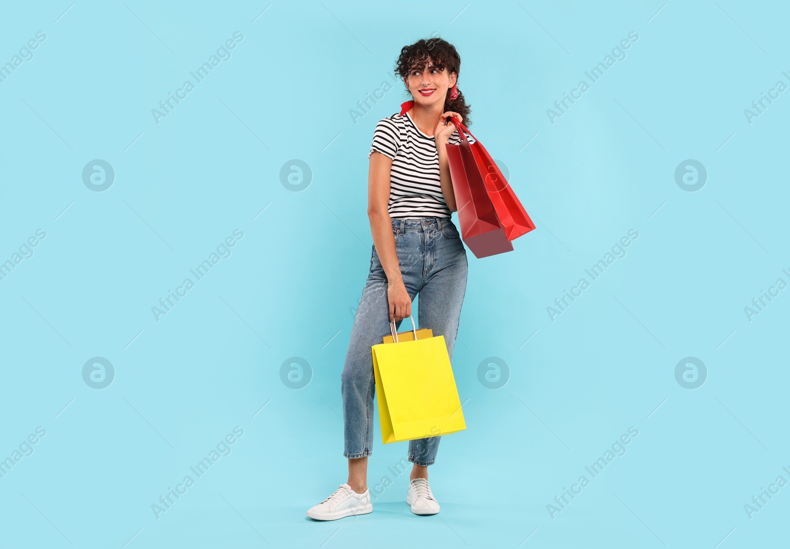 Photo of Smiling woman with colorful shopping bags on light blue background