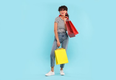 Smiling woman with colorful shopping bags on light blue background