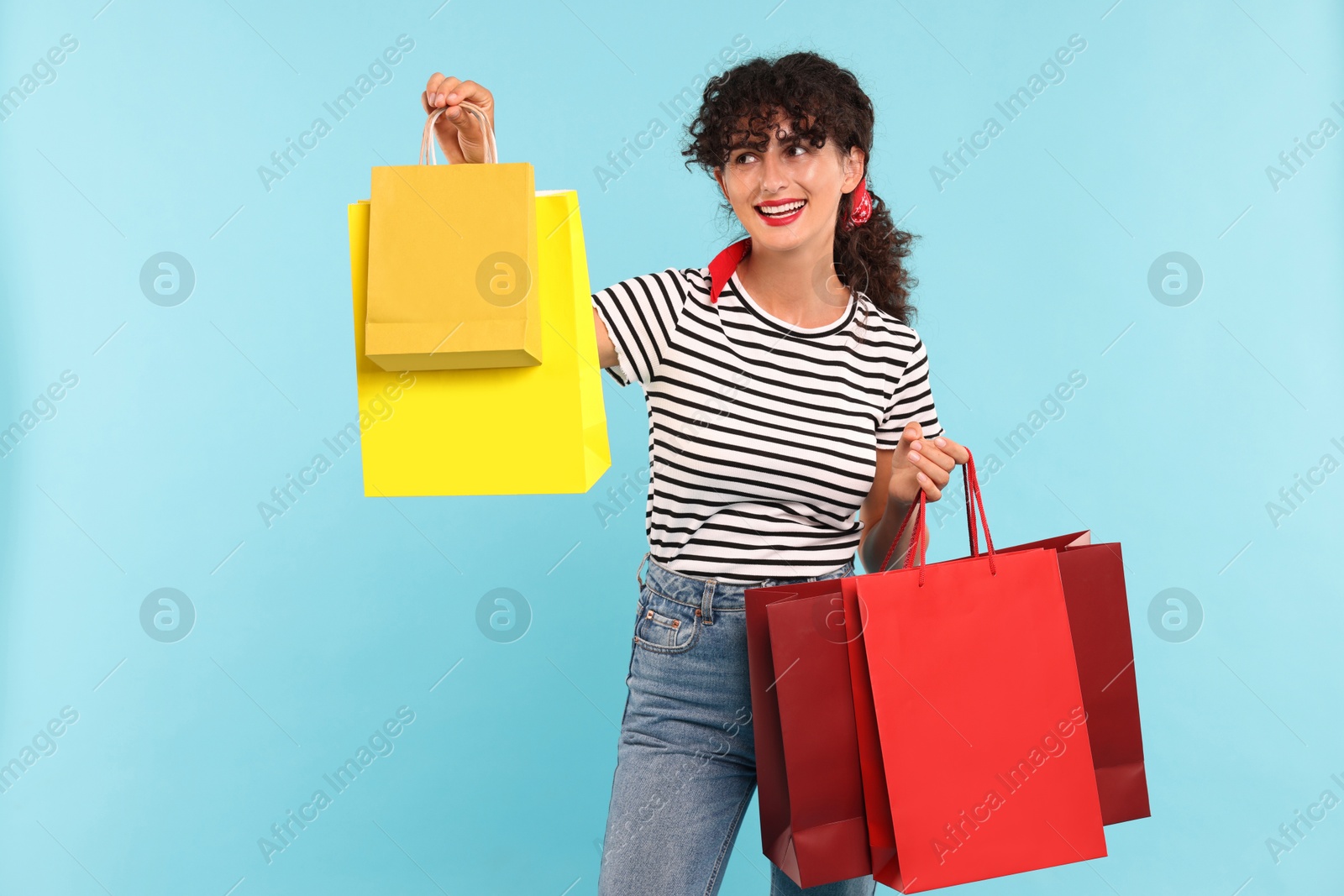 Photo of Smiling woman with colorful shopping bags on light blue background