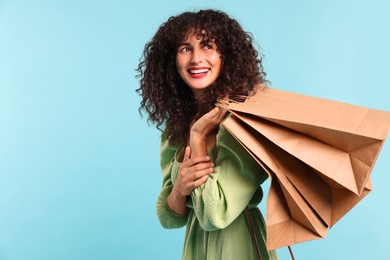 Smiling woman with shopping bags on light blue background. Space for text