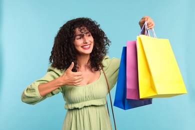 Photo of Smiling woman with colorful shopping bags showing thumbs up on light blue background