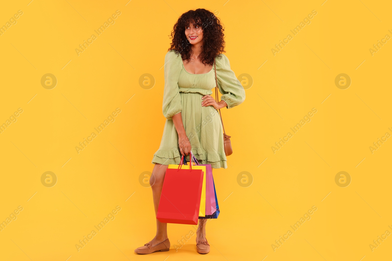 Photo of Smiling woman with colorful shopping bags on yellow background. Space for text