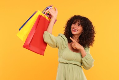 Smiling woman pointing at colorful shopping bags on yellow background