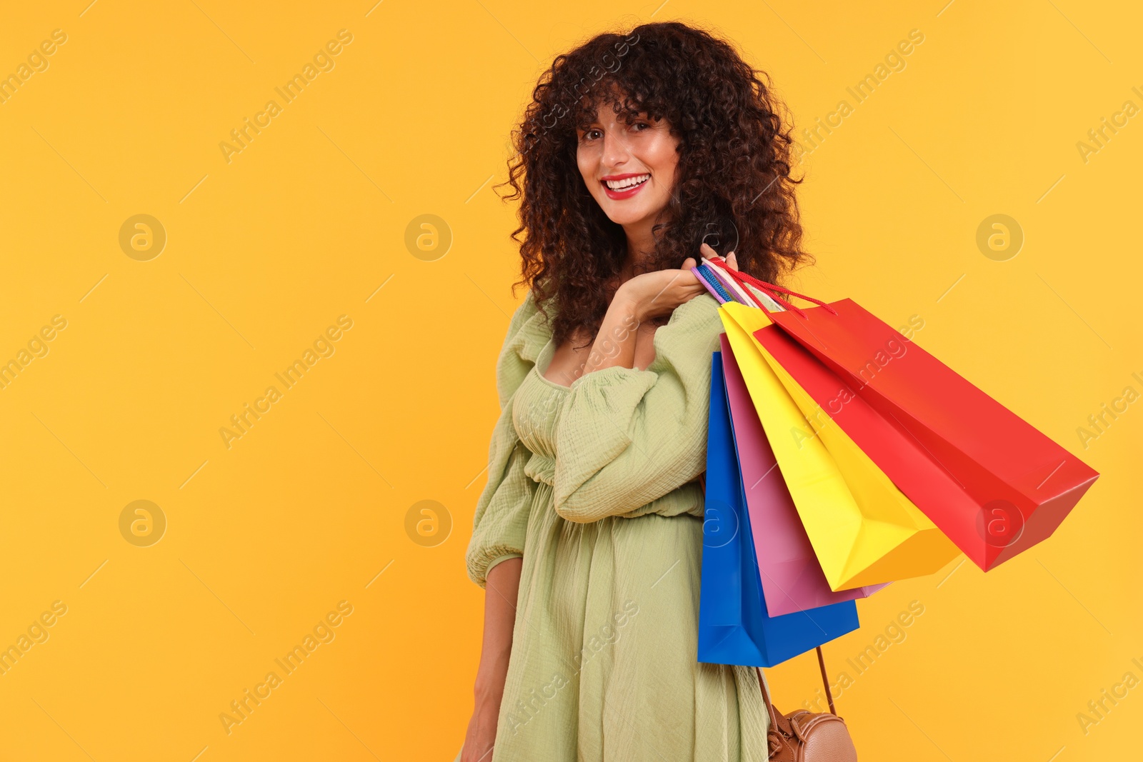 Photo of Smiling woman with colorful shopping bags on yellow background. Space for text