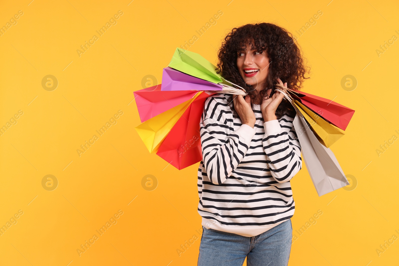 Photo of Smiling woman with colorful shopping bags on yellow background. Space for text