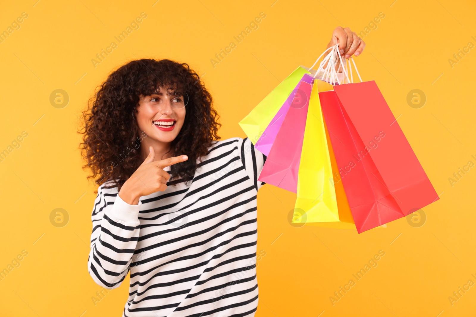 Photo of Smiling woman pointing at colorful shopping bags on yellow background