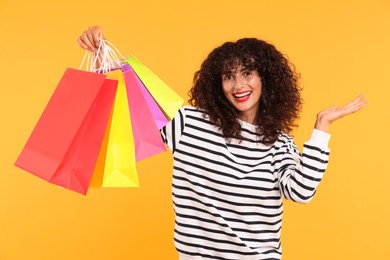 Happy woman with colorful shopping bags on yellow background