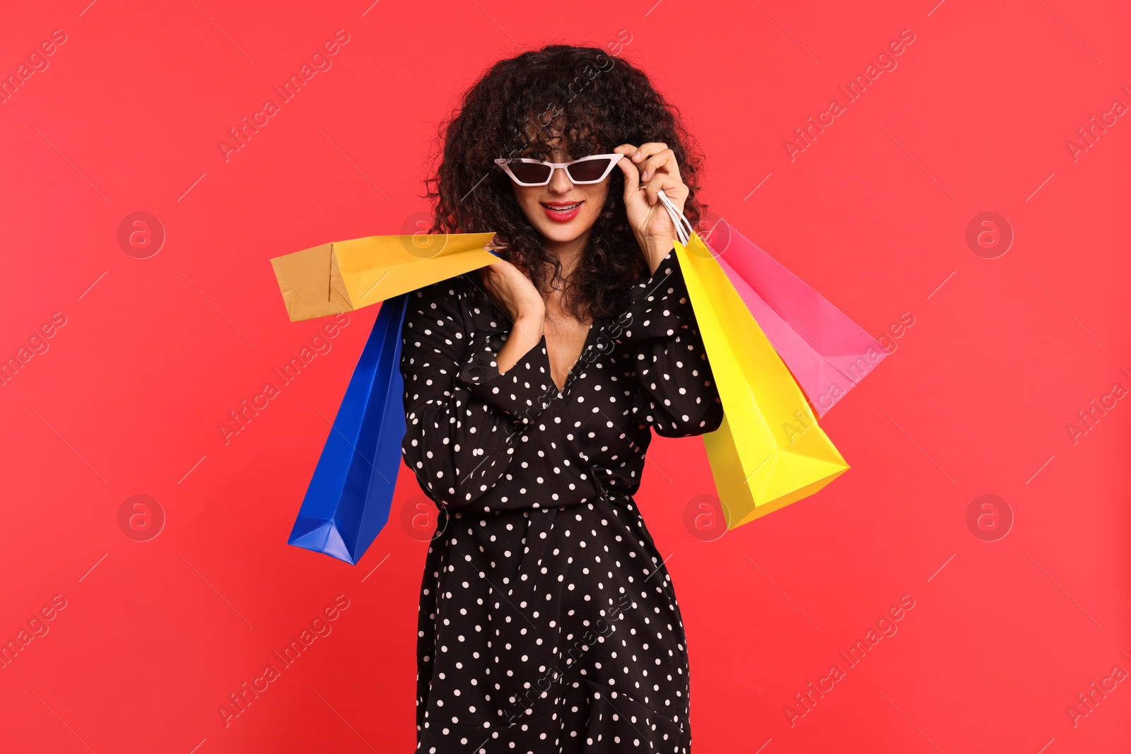 Photo of Smiling woman with colorful shopping bags on red background