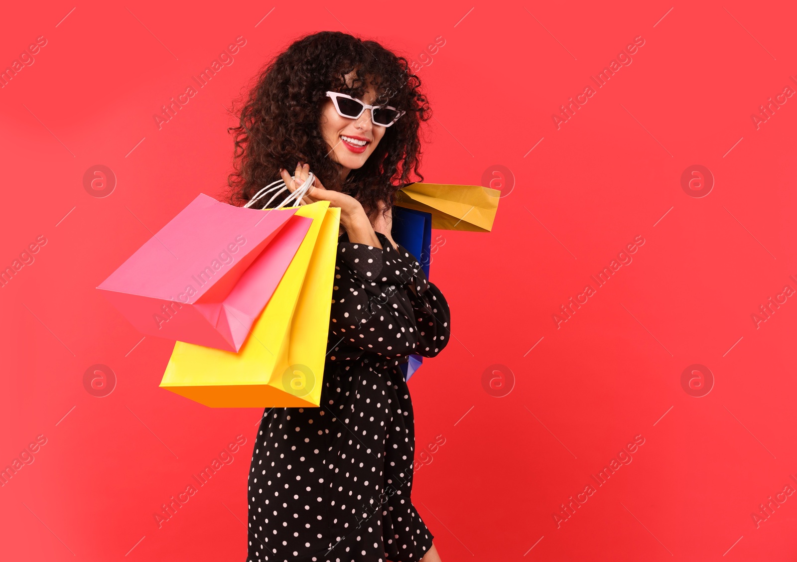 Photo of Smiling woman with colorful shopping bags on red background. Space for text