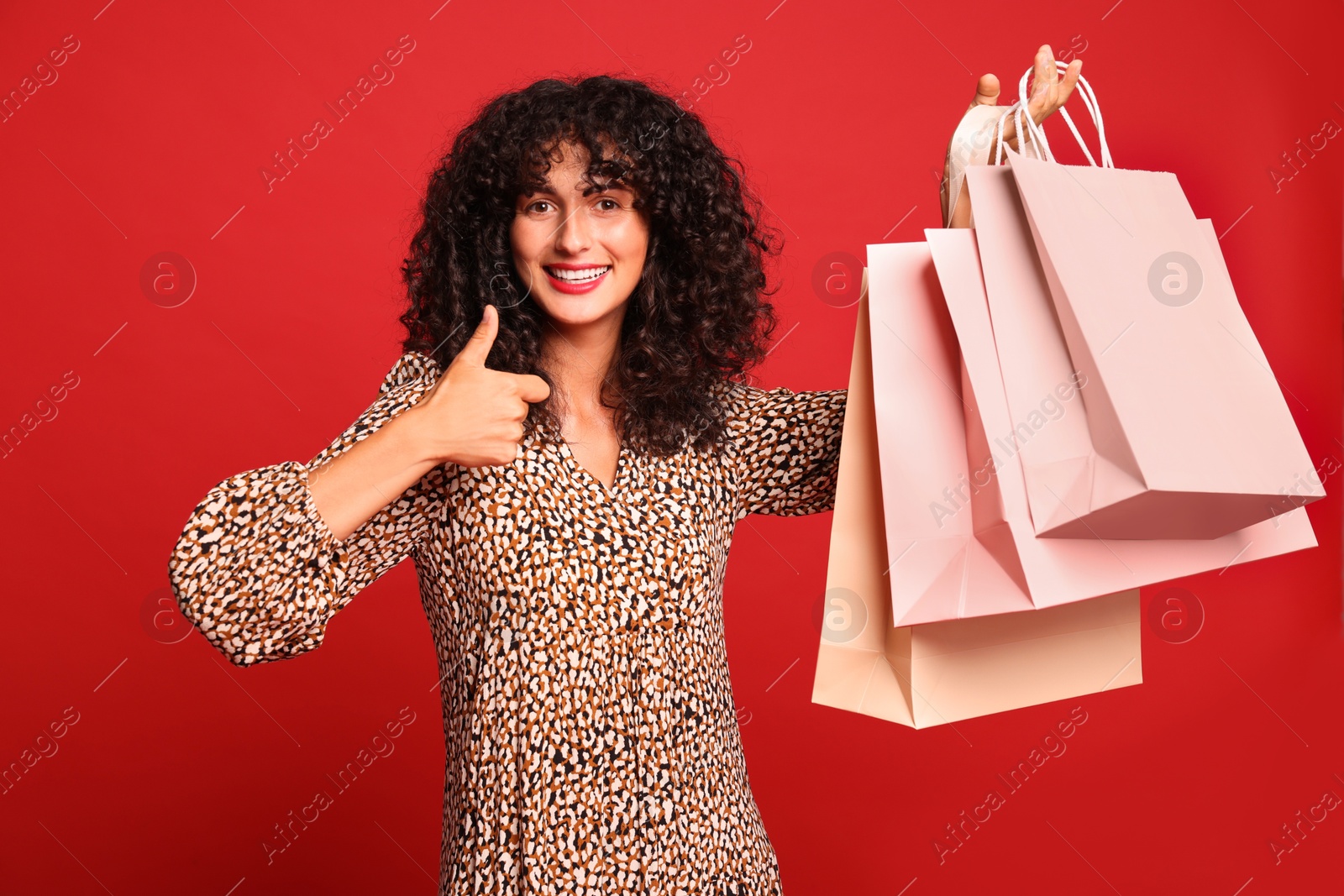 Photo of Smiling woman with shopping bags showing thumbs up on red background