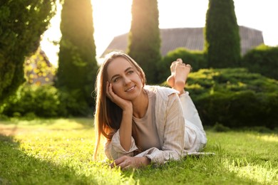 Happy woman resting on green lawn in park