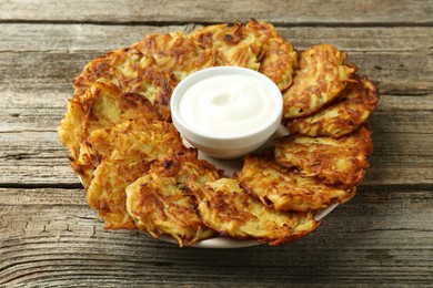 Photo of Delicious potato pancakes and sour cream on wooden table, closeup