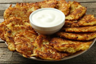 Photo of Delicious potato pancakes and sour cream on wooden table, closeup