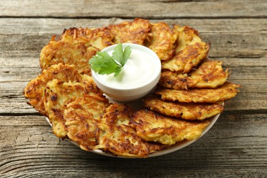 Delicious potato pancakes, sour cream and parsley on wooden table, closeup