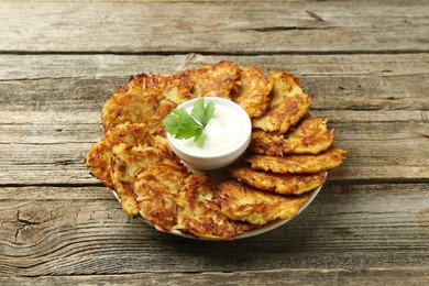 Delicious potato pancakes, sour cream and parsley on wooden table