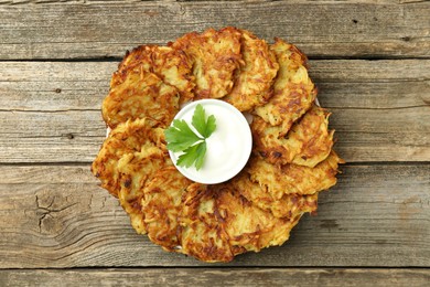 Photo of Delicious potato pancakes, sour cream and parsley on wooden table, top view