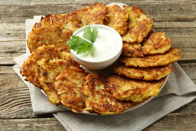 Photo of Delicious potato pancakes, sour cream and parsley on wooden table, closeup