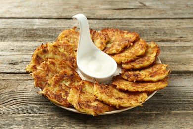 Photo of Delicious potato pancakes and sour cream on wooden table, closeup