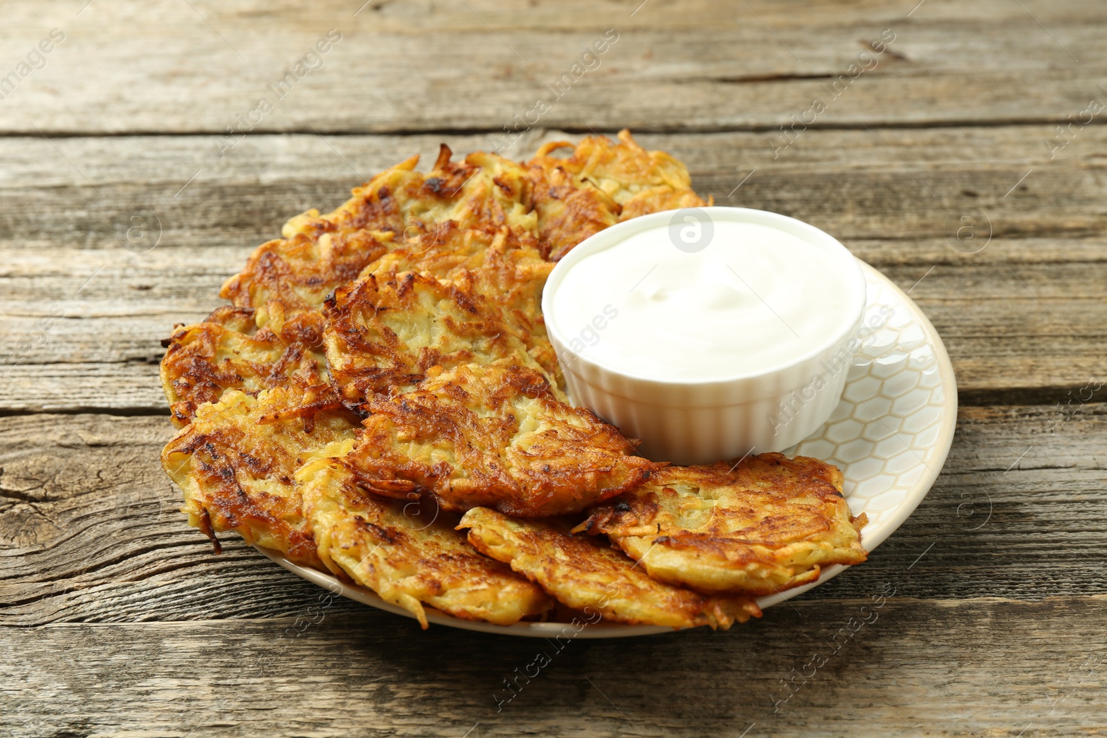 Photo of Delicious potato pancakes and sour cream on wooden table, closeup