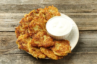 Photo of Delicious potato pancakes and sour cream on wooden table, closeup