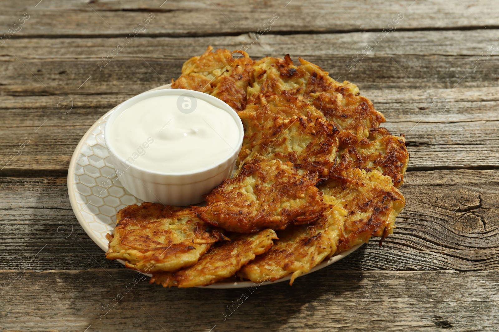 Photo of Delicious potato pancakes and sour cream on wooden table, closeup