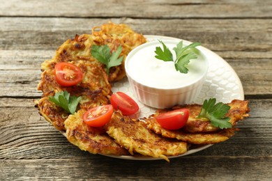 Photo of Delicious potato pancakes, sour cream, tomatoes and parsley on wooden table, closeup