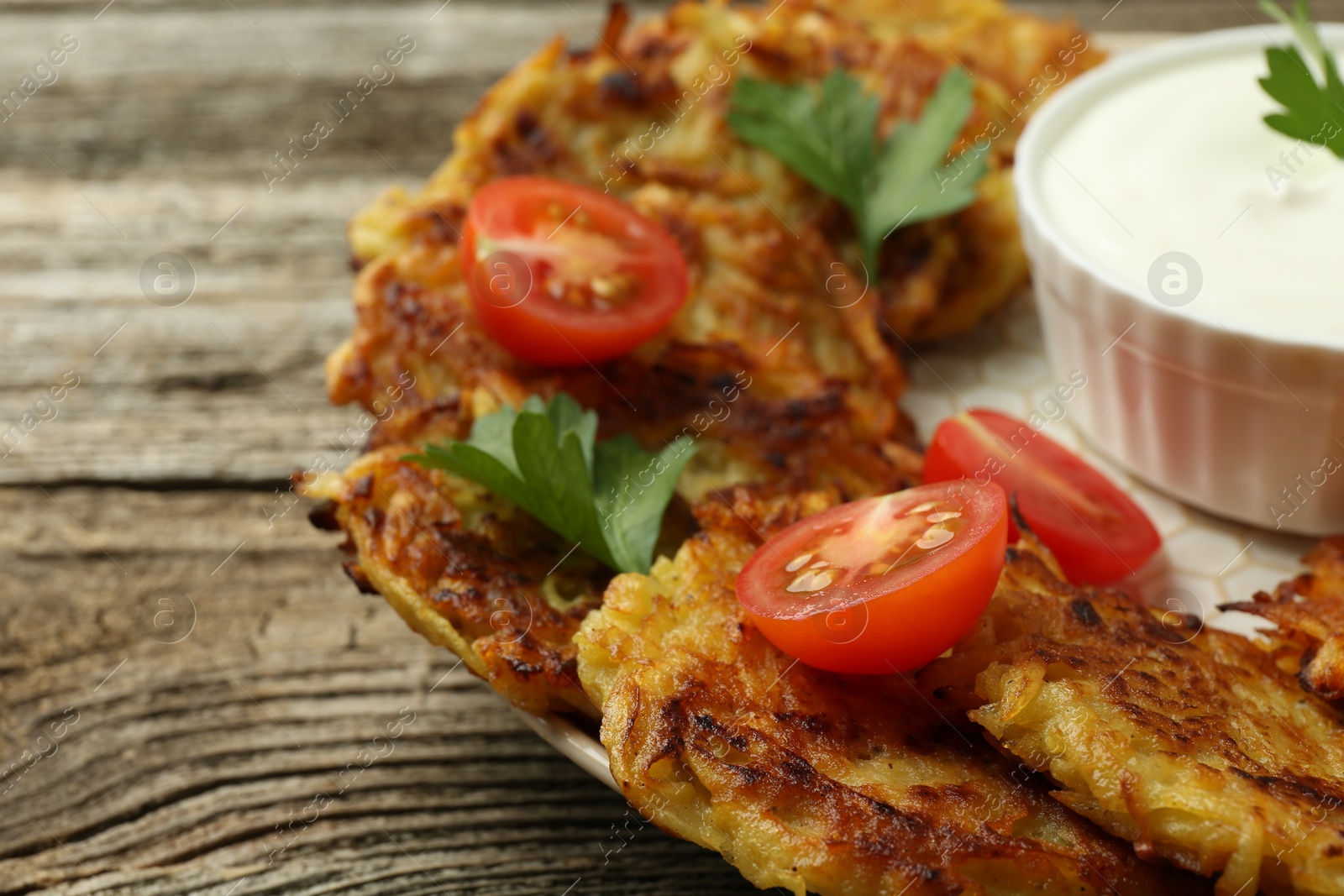 Photo of Delicious potato pancakes, sour cream, tomatoes and parsley on wooden table, closeup