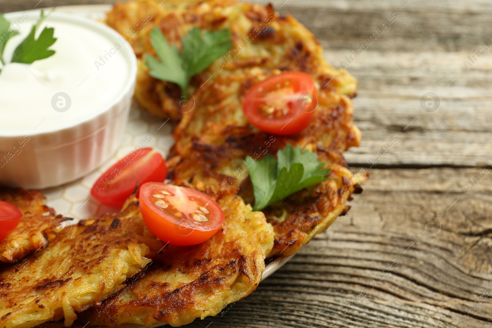 Photo of Delicious potato pancakes, sour cream, tomatoes and parsley on wooden table, closeup