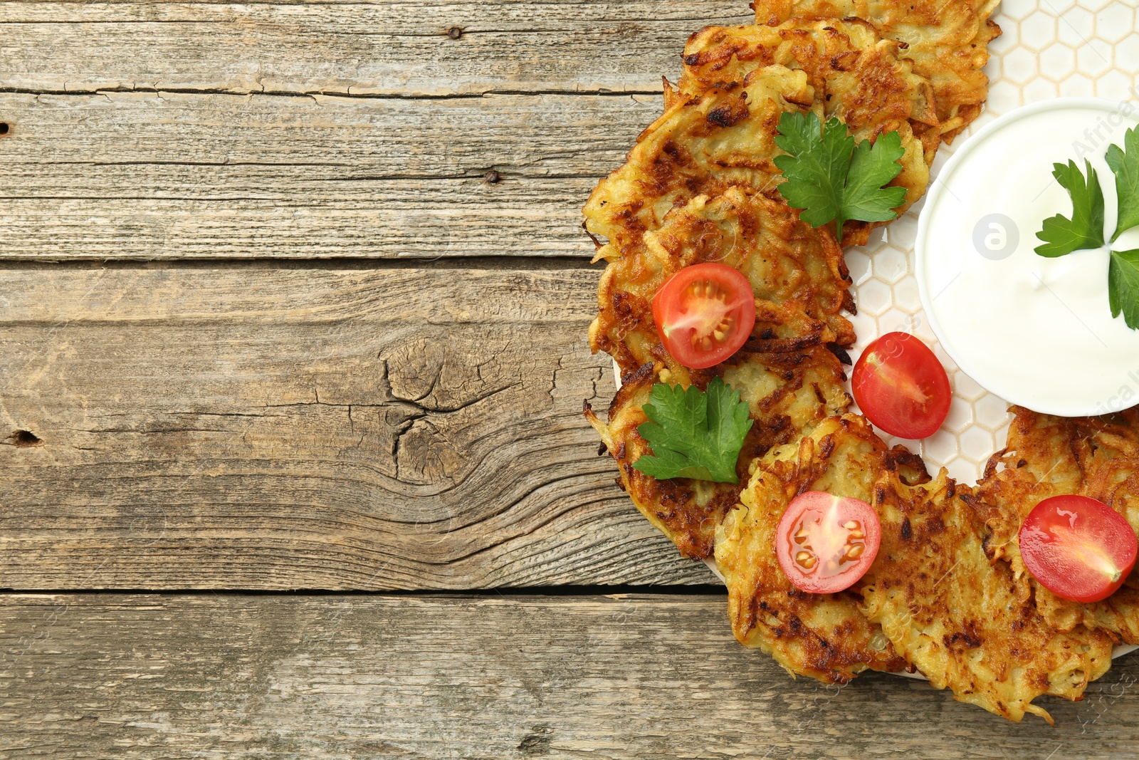 Photo of Delicious potato pancakes, sour cream, tomatoes and parsley on wooden table, top view. Space for text