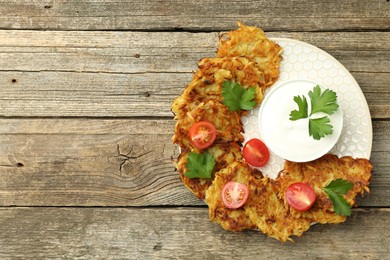 Photo of Delicious potato pancakes, sour cream, tomatoes and parsley on wooden table, top view. Space for text