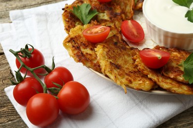 Photo of Delicious potato pancakes, sour cream, tomatoes and parsley on wooden table, closeup