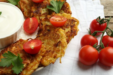 Photo of Delicious potato pancakes, sour cream, tomatoes and parsley on table, closeup