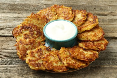 Photo of Delicious potato pancakes and sour cream on wooden table, closeup