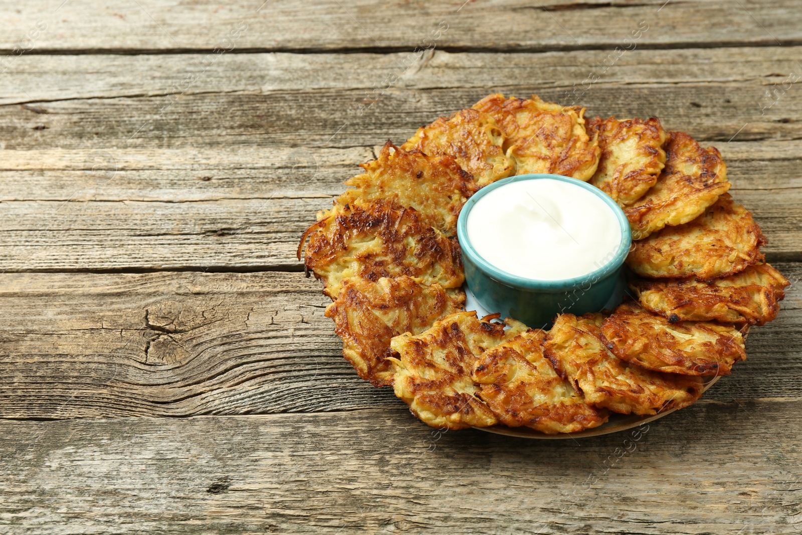 Photo of Delicious potato pancakes and sour cream on wooden table. Space for text