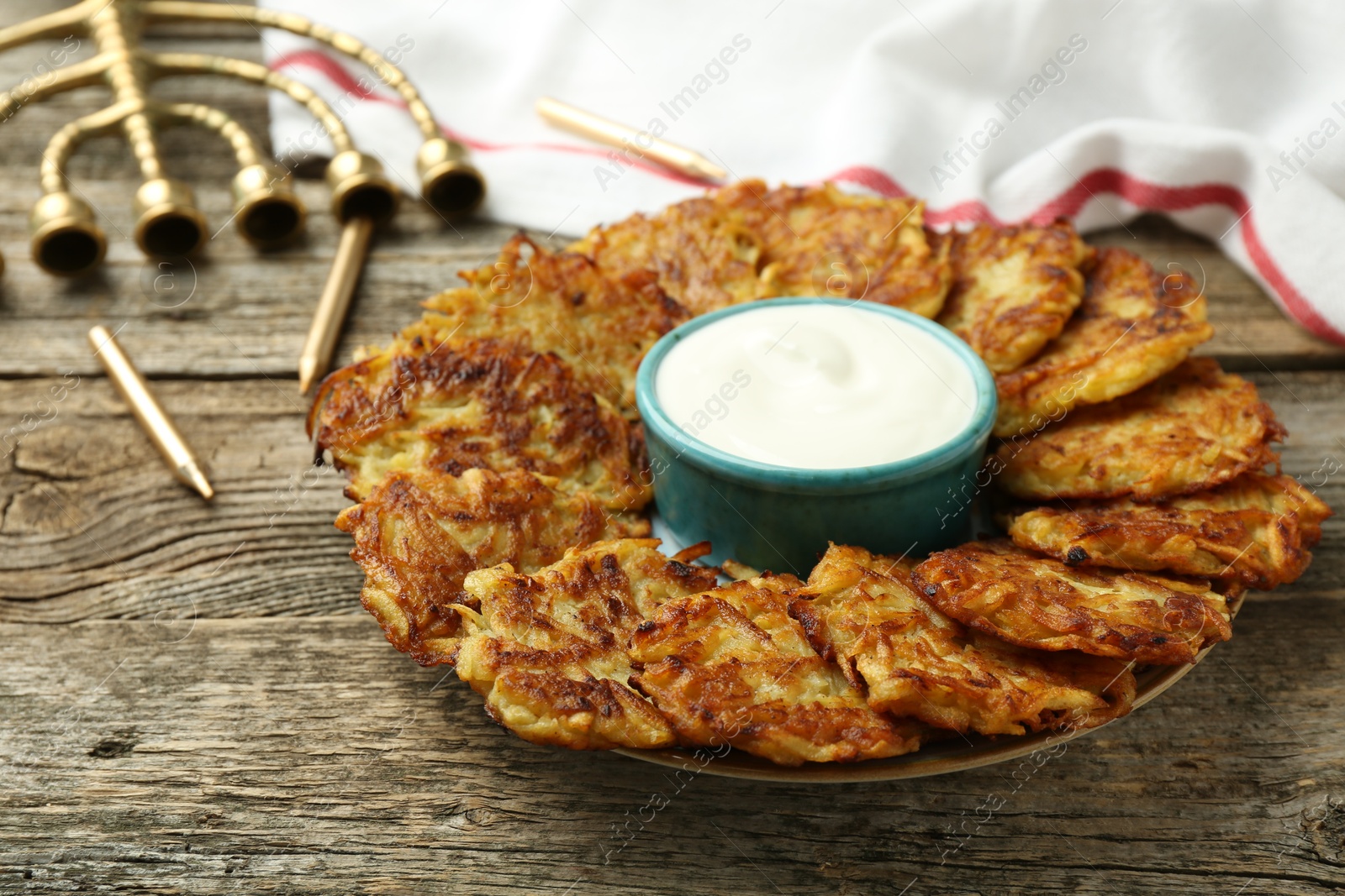 Photo of Delicious potato pancakes, sour cream, menorah and candles on wooden table, closeup. Hanukkah festive food