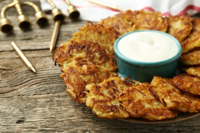 Photo of Delicious potato pancakes, sour cream, menorah and candles on wooden table, closeup. Hanukkah festive food